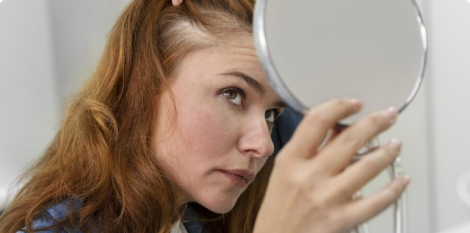 Femme en train d'examiner avec un miroir son cuir chevelu